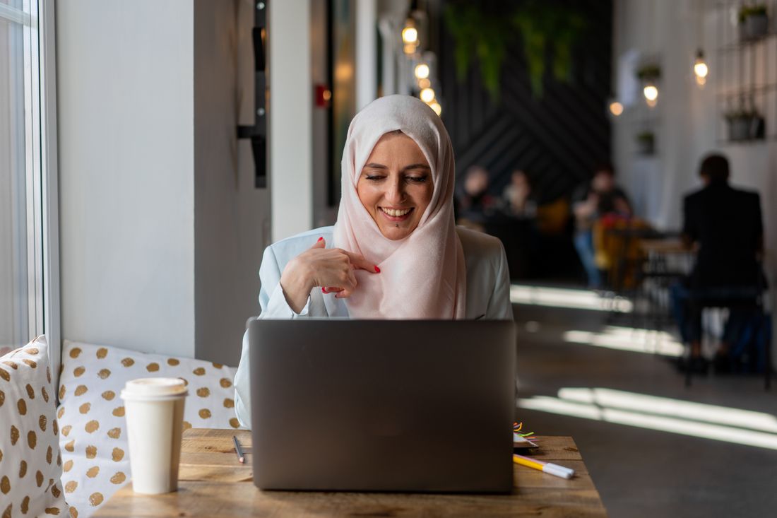 Lächelnde Frau mit Kopftuch arbeitet am Laptop